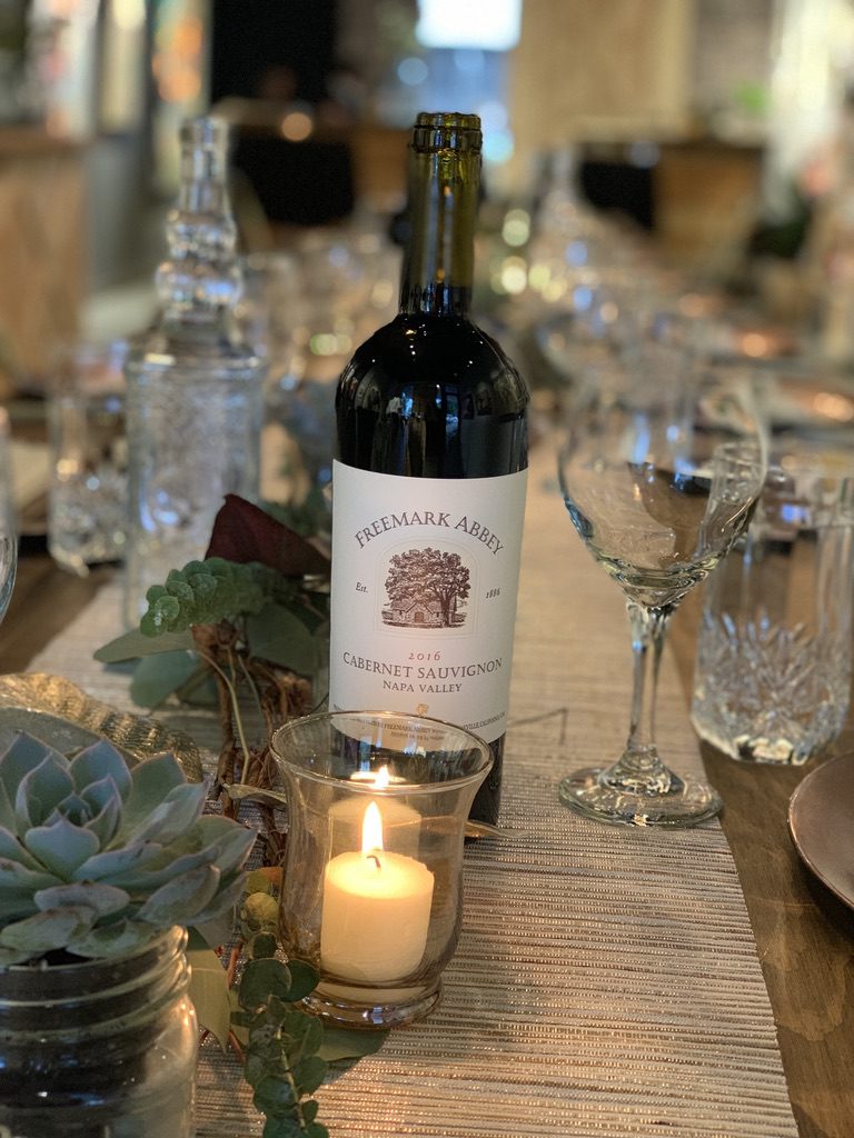 Wine bottle, candle, and glasses on table.